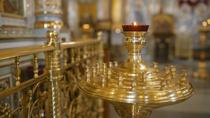 Burning red votive candle stands on a golden brass candelabrum in a church