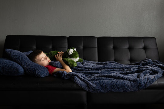 Child sleeping on sofa with plush toy under a blue blanket