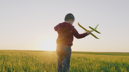 Child Boy Runs Through Park With Toy Plane His Hand Sunset Sky. Carefree Small Boy Jogging With Airplane Through Meadow. Dreaming Flights Enjoying Summer Vacation. Steadicam Shot.