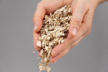 Hands pouring uncooked raw oatmeal on a gray background.
