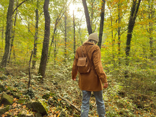 A woman is walking through a forest wearing a brown coat and a backpack