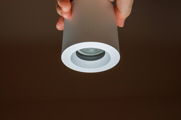 Close-up of a minimalist cylindrical LED light fixture held by a hand, showcasing its modern design...