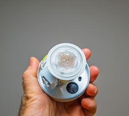 Hand holding a compact LED light fixture with wiring and connectors visible, showcasing details of the bulb and hardware in a clean, minimalist setting