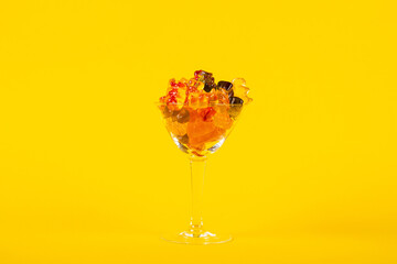 Fruit flavored worm shape, jelly candies in a glass on yellow background.