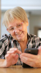 Senior woman smiling as she uses her smartphone, enjoying a moment of technology engagement indoors.