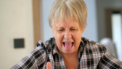 Elderly woman making a disgusted face with her tongue out, expressing strong dislike.