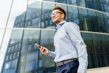 Professional Man in Light Blue Shirt Walking Outside a Modern Office Building While Using a Smartphone