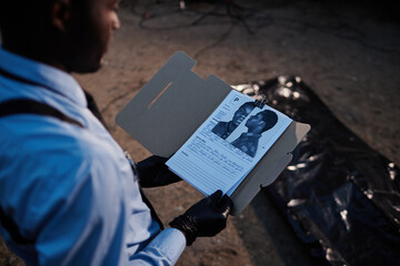 Over shoulder view of African American man as police officer looking at identikit of potential...