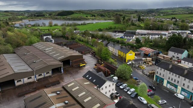 Ballybay Town, County Monaghan, Ireland, April 2024. Drone tracks left above the rooftops near Castleblayney road towards Lough Major lake revealing a rural landscape in background under rainy clouds.