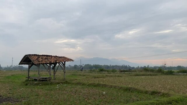 small wooden hut  is situated in a field of  grass , with  a cloudy sky overhead 