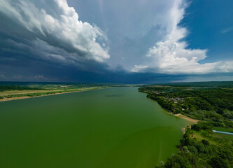 Panorama with a storage dam captur with a drone in the countryside. A calm river that comes from the mountains among the green forests and flows into the lake at the edge of a village in Romania