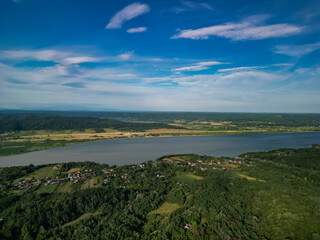 Panorama with a storage dam captur with a drone in the countryside. A calm river that comes from the mountains among the green forests and flows into the lake at the edge of a village in Romania