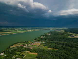 Obraz premium Panorama with a storage dam captur with a drone in the countryside. A calm river that comes from the mountains among the green forests and flows into the lake at the edge of a village in Romania