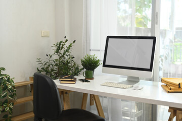 Obraz premium Contemporary workspace with a white computer monitor, plants and natural light