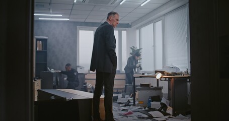 Office robbery case: Crime investigation team working. Male detective examines crime scene, female...