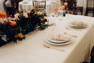 A wedding table with a luxurious floral arrangement in peach tones and elegant white place settings.