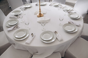 A round wedding table set with white plates, cutlery and glasses.