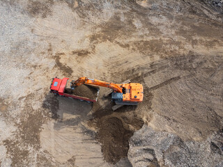 Aerial view of an excavator loading sand into a truck on a sunny day, top view. Shooting from a...