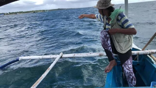 young man is fishing with a handline from a boat in deep sea waters.