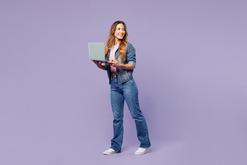 Naklejka premium Full body young IT woman wear denim jacket violet top casual clothes hold use work on laptop pc computer look aside isolated on plain pastel light purple background studio portrait. Lifestyle concept.