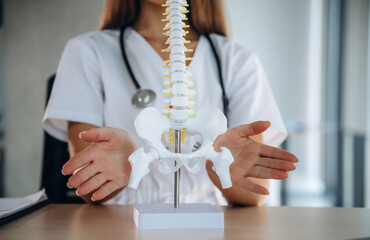 Obraz premium Showing the spine model that is on the table. Professional female doctor in the clinic indoors