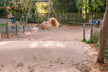 beautiful adorable red-haired excited happy smiling child girl swinging on a rope sling on an...