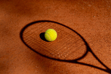 close up shadow on professional tennis court with red clay surface tennis ball lies on tennis racket professional equipment