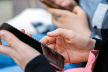 Closeup of young people hands holding mobile phones. Two teenager girls are using their smartphones outdoors, texting or browsing. Selective focus. Copy space