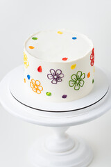 Birthday cake with white cream cheese frosting decorated with colorful buttercream flowers drawings. White background