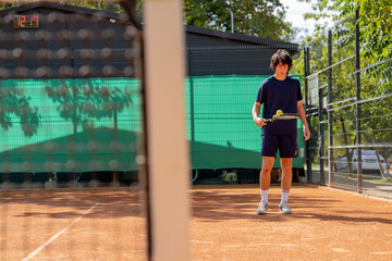 Obraz premium professional tennis court young curly guy trains hitting the ball with tennis racket professional preparation for the game