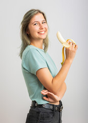 Young cheerful woman eating a banana. Isolated on gray background
