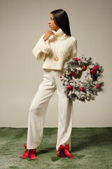 A young woman displays her winter style, holding a festive red accented wreath.