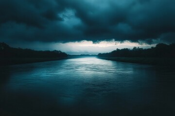 Obraz premium A wide river flows beneath dark, stormy skies creating a dramatic and moody atmosphere with an ethereal glow of light breaking through in the distance.