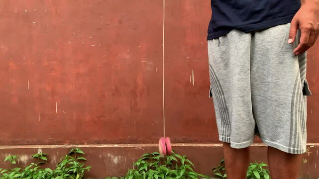 4K video of male hand playing yoyo. A yoyo is a toy consisting of two disks connected by an axle around which a string is wound. A yoyo is thrown down on a string and can be returned to the hand