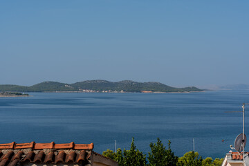 Peaceful coastal scene overlooking calm blue sea waters and green islands under clear sky.