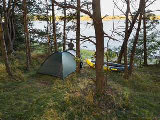 Outdoor activities, man with tent and rubber boat on an island in the Aegna forest on a summer day.