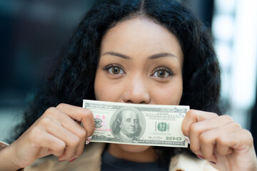 Close-up of a woman holding a hundred-dollar bill in front of her face, symbolizing themes of money, finance, and wealth.