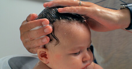 Fototapeta premium Hands gently massaging shampoo into a baby’s scalp during bath time, slow motion at 800 fps, close-up of a tender moment of care and nurturing