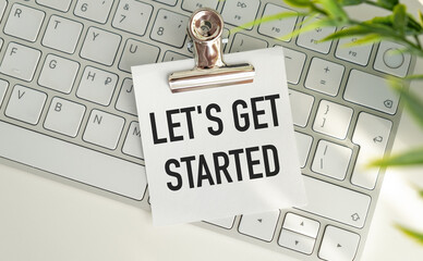 Let's Get Started- text written on sticky note lying on the keyboard with office background