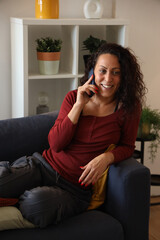 Obraz premium Happy woman talking on phone at home, relaxing on sofa