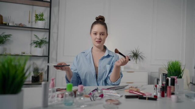 Portrait of makeup artist and blogger filming review on eyelash curler in blog. Young female beauty influencer streaming in social media, looking at camera and talking, trendy makeup video tutorial