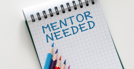 MENTOR NEEDED text on a sticky on notebook with pen and glasses , white background