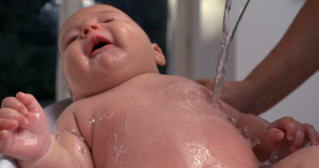 Water pouring over baby’s chest during bath, baby tilting head and looking calm, relaxing bath...