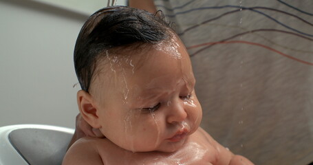 Water pouring over baby’s head during bath, baby calm and eyes closed, intimate and serene bath...