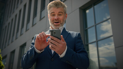 Caucasian happy euphoric mature middle-aged business man celebrate mobile win excited overjoyed...