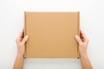 Young adult woman hands holding closed brown carton box on light gray table background. Closeup....