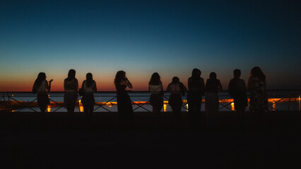 Fototapeta premium Young people talking and watching the sunset over the sea