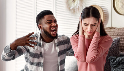 Fototapeta premium African american husband yelling at european wife. Woman covers ears