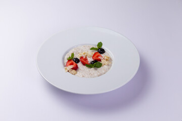 Milk porridge with berries in a plate on a white background.