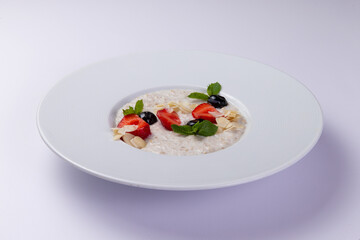 Milk porridge with berries in a plate on a white background.